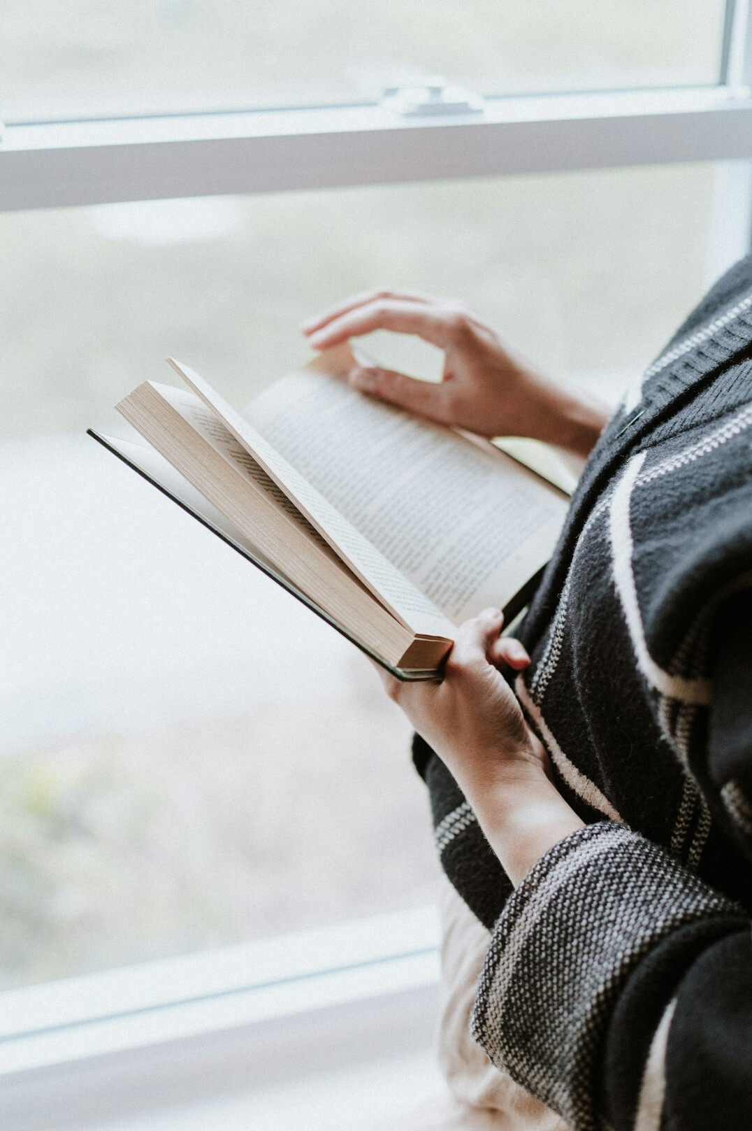Persona leyendo un libro junto a una ventana con una taza de café